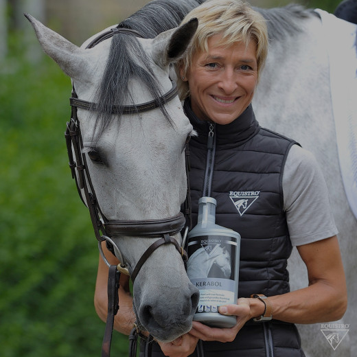 Ingrid Klimke hält Equistro Produkt neben weißem Pferd